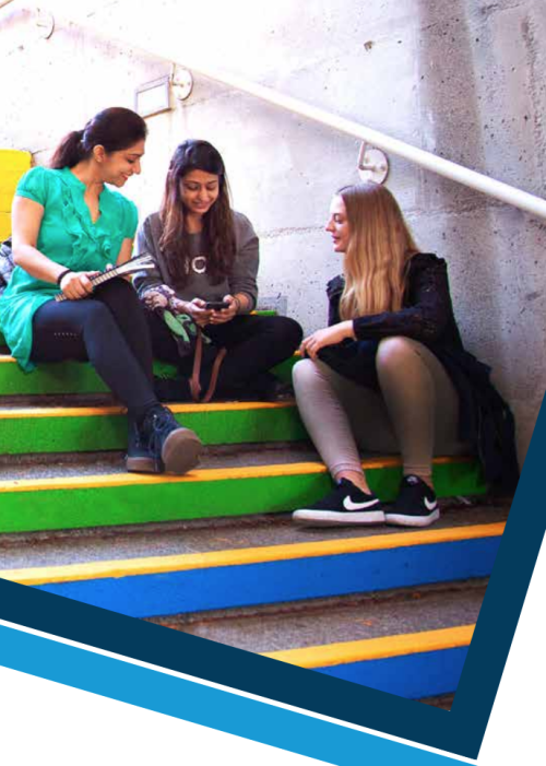 students seated on a stairwell painted with rainbow colours