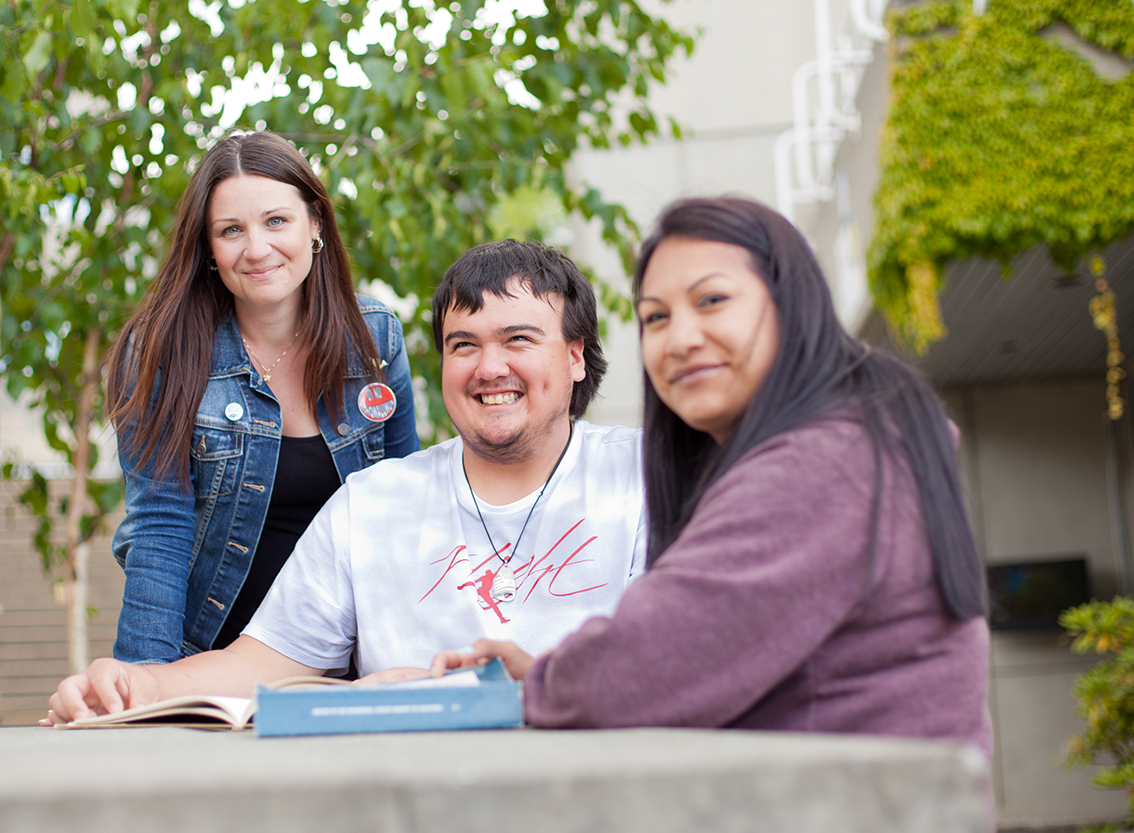 two young woman sit with a young man at a table outdoors